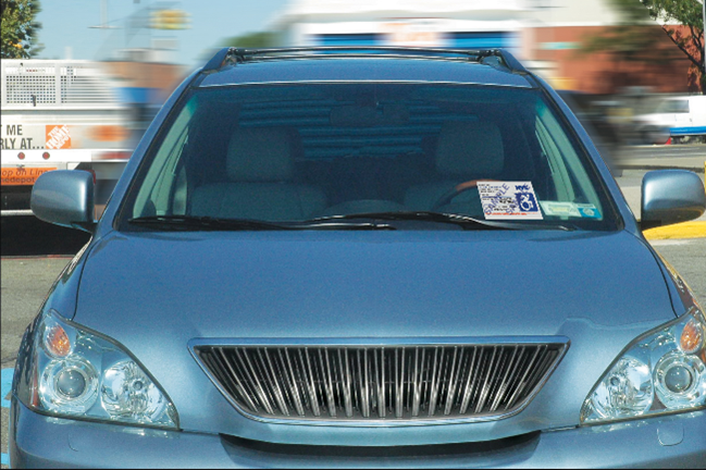 A blue car is parked with a parking placard on the driver’s side dashboard.
