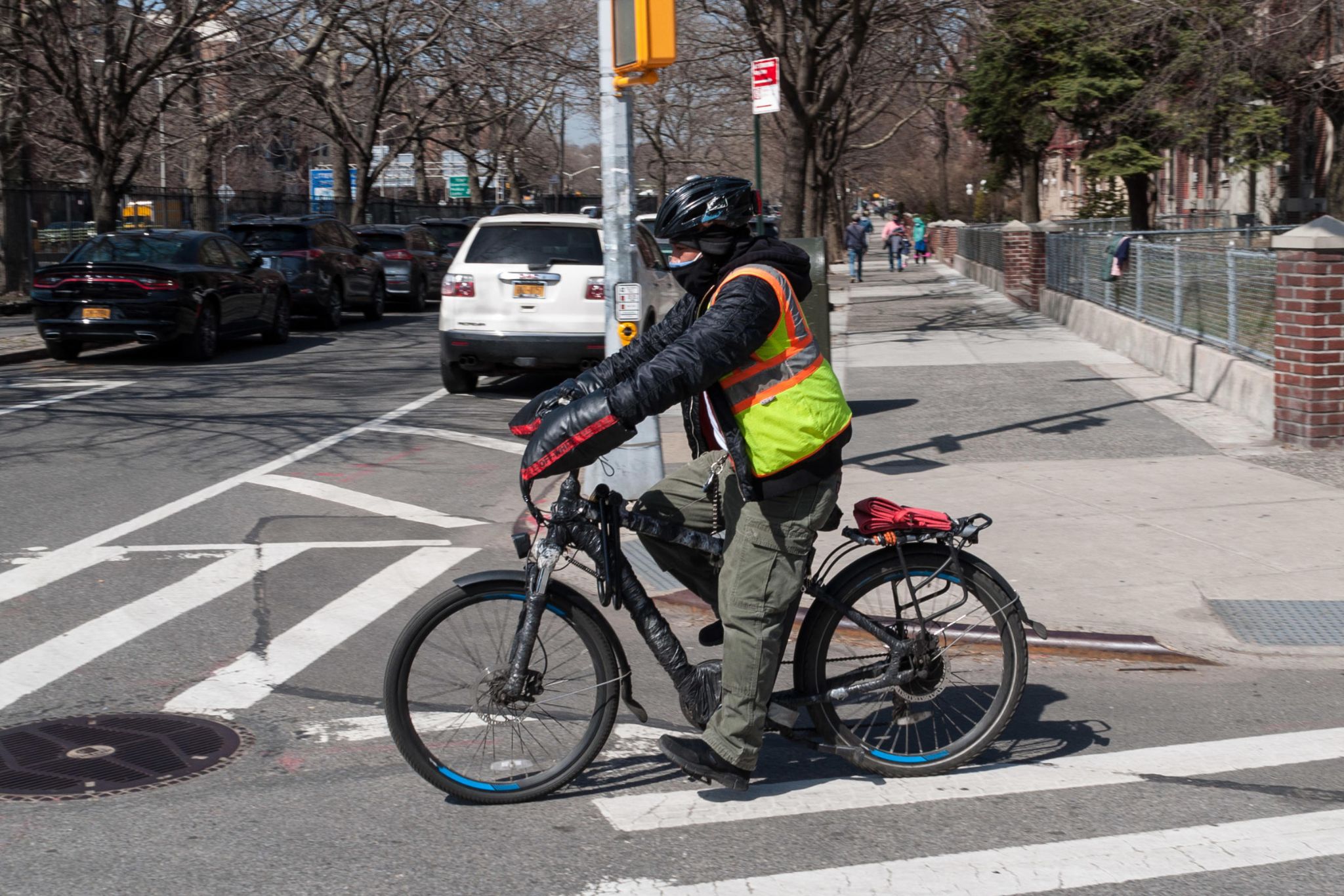 A delivery worker wearing a bike helmet and bright vest rides an e-bike in Brooklyn.