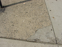 Close up of a sidewalk piece that has a corner filled in with concrete, creating a patchwork of sidewalk materials.