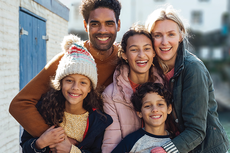 Portrait of a diverse family with their arms around each other in an outdoor setting.
                                           