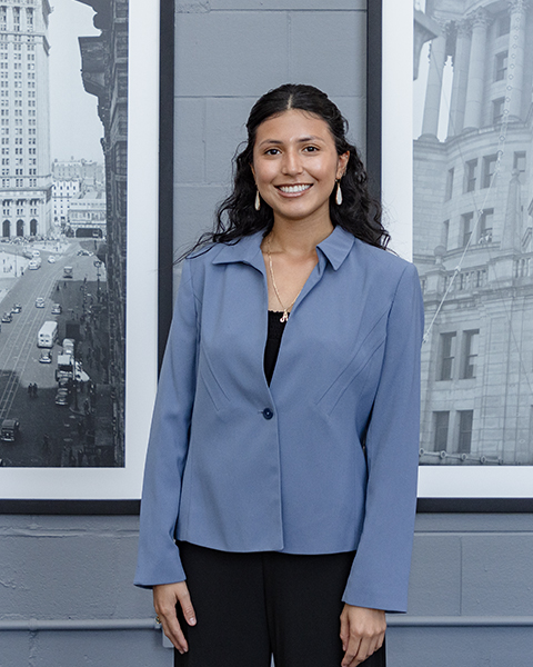 Woman smiling, wearing a blue blazer and black pants.