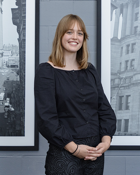 Woman smiling, wearing a black shirt and black patterned pants.