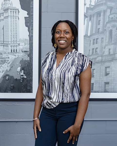 Woman smiling, wearing a navy blue and white patterned blouse and navy blue pants.