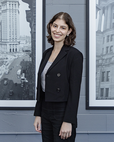 Woman smiling, wearing a short black blazer and black pants.