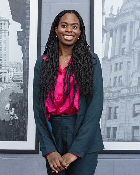 Woman smiling, wearing a grey blazer and grey pants.