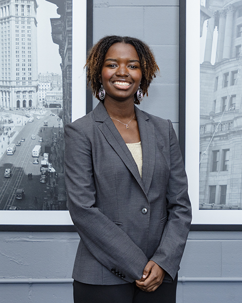 Woman smiling, wearing a grey blazer and black pants.