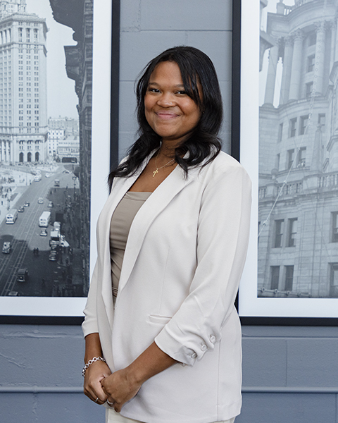 Woman smiling, wearing a white blazer and taupe shirt.