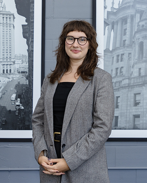 Woman smiling, wearing glasses and a grey blazer.