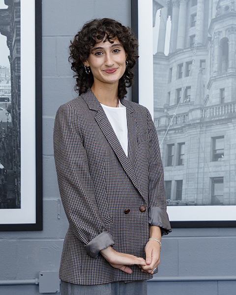 Woman smiling, wearing a houndstooth patterned blazer and white shirt.