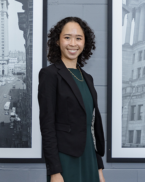 Woman smiling, wearing a green dress with black blazer.