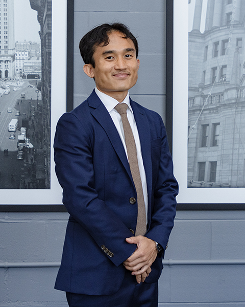 Man smiling, wearing a blue blazer with taupe tie.