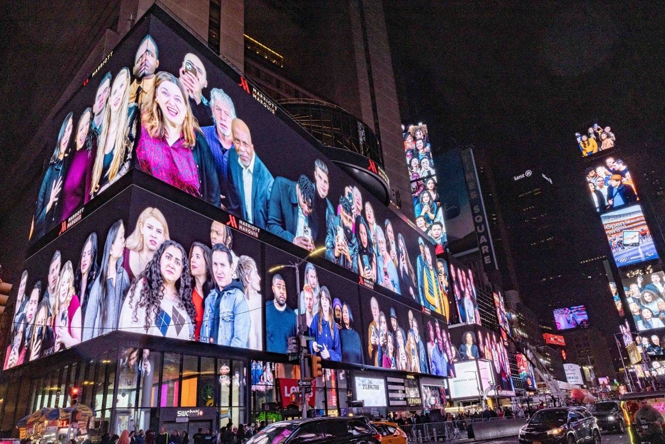 An installation on the screens of Times Square with people appearing to gawk at passersby. 