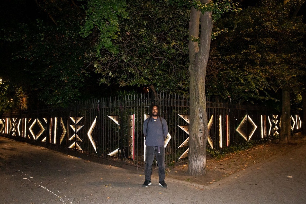 Oni stands in front of his fence lighting installation titled Halo.  