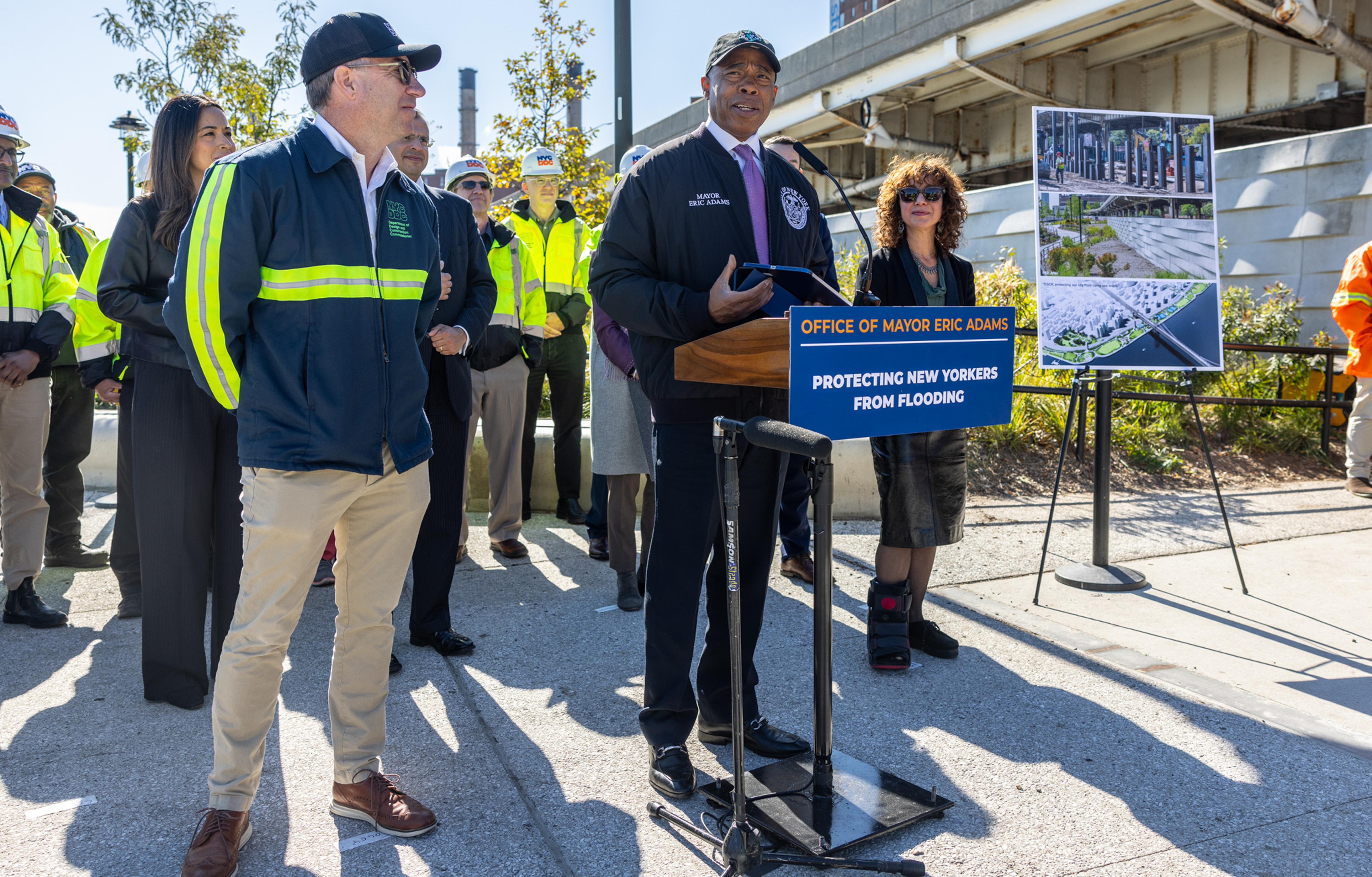 Mayor Adams stands with DDC Commissioner Foley and Deputy Mayor Joshi behind the podium at event outside
                                           