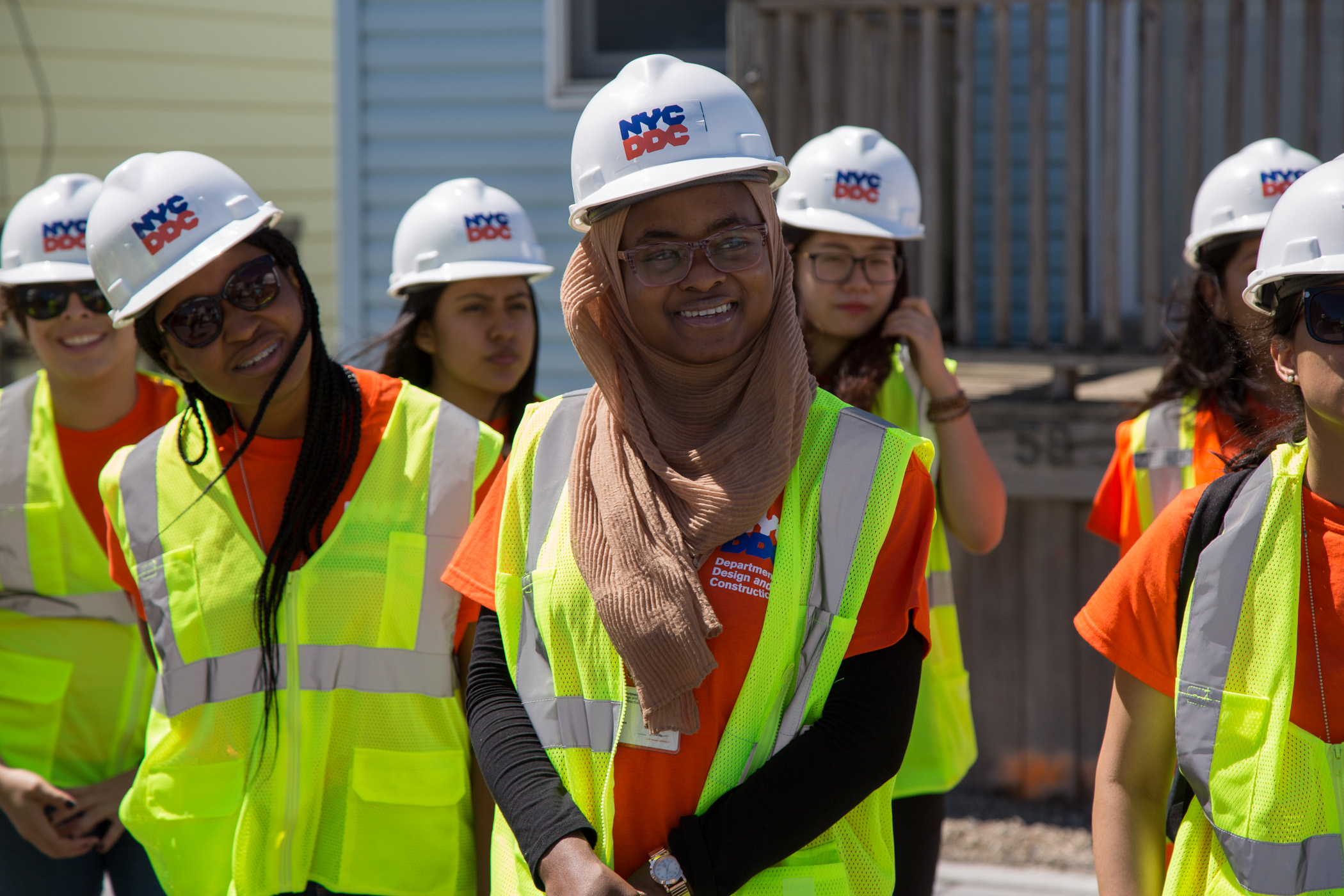 interns at a project site wear construction helmets and vests