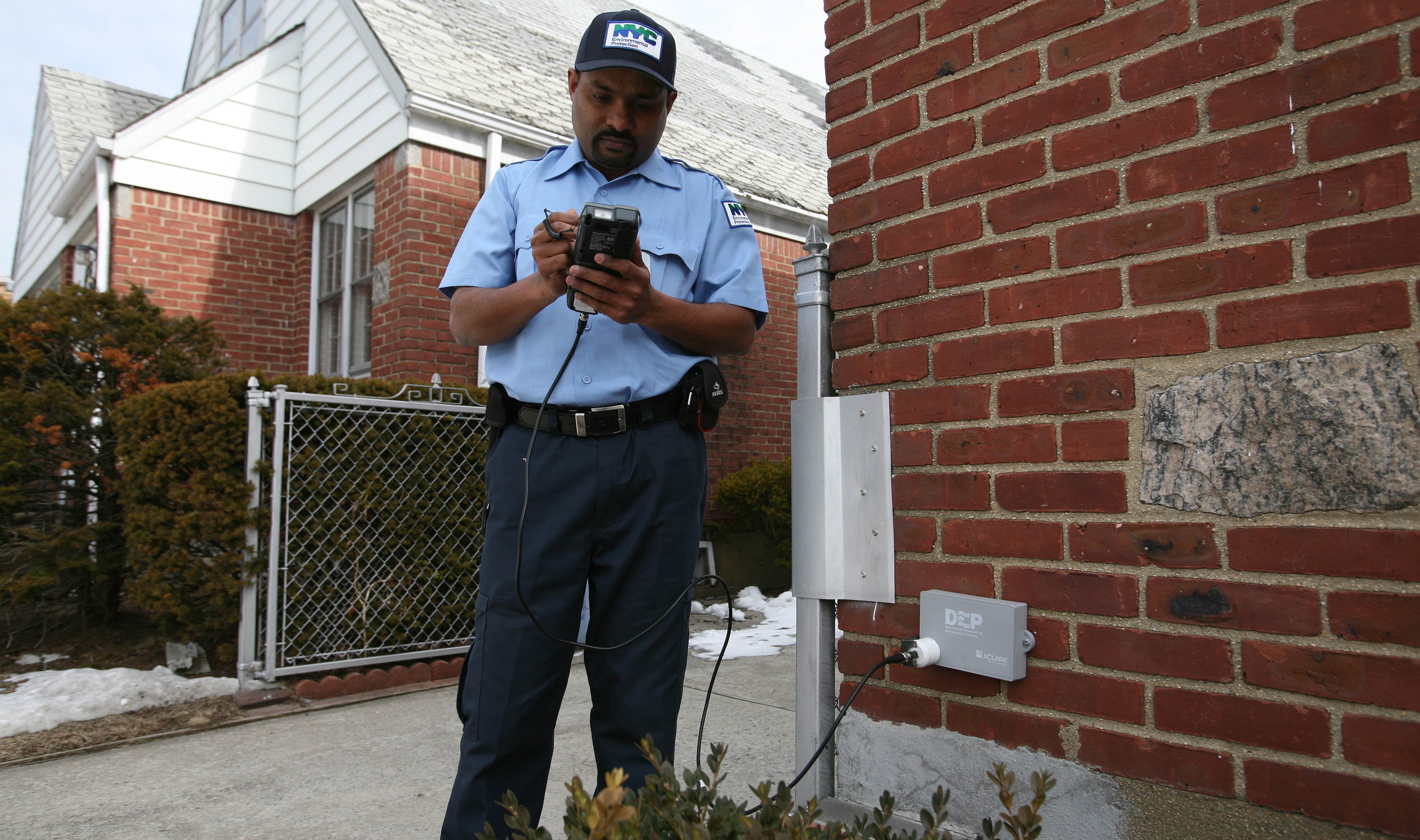 An image of a uniformed DEP employee with a badge checking an AMR device that is attached to the side of a property