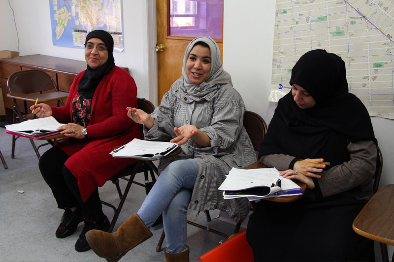 three women sitting in classroom talking and working on worksheets