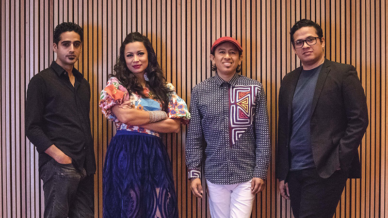 Group of performers, three men and one woman posing in front of natural wooden pillared wall