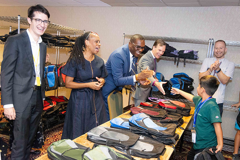 Photo of backpacks on a table and staff giving them away