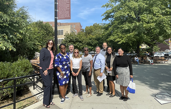 Nine people standing outside under a historic district marker, smiling