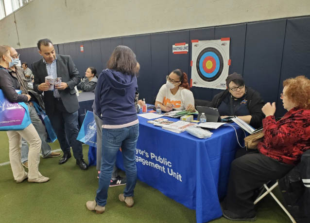 PEU Specialists sit at a PEU table, which has flyers on it, and talk to senior New Yorkers who have approached their table.