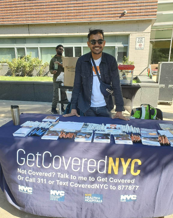 Specialist leaning against table smiling at the camera wearing sunglasses and a PEU T-Shirt with a button down over it. Table cloth reads 