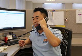 Man sits in office desk wearing a light blue PEU polo while on a landline phone.