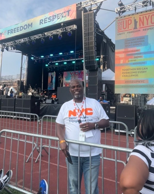 PEU Outreach Specialist wearing a PEU T-shirt stands outside behind the concert barriers as he smiles