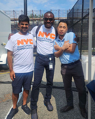 Three PEU staff stand smiling at the camera, wearing their PEU shirts