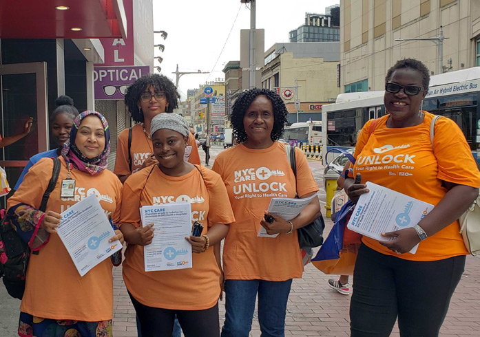 5 staff wear orange t-shirts that say NYC Care Unlock. They hold flyers as they pose for the camera.