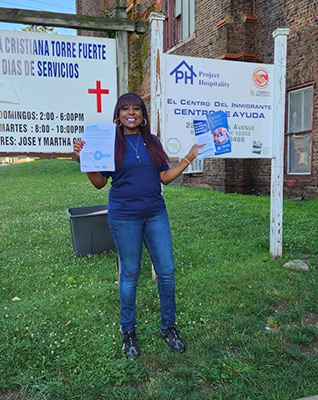 Woman stands outside holding flyers, smiling