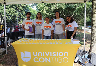 5 staff wear orange t-shirts that say NYC Care Unlock. They hold flyers as they pose for the camera.