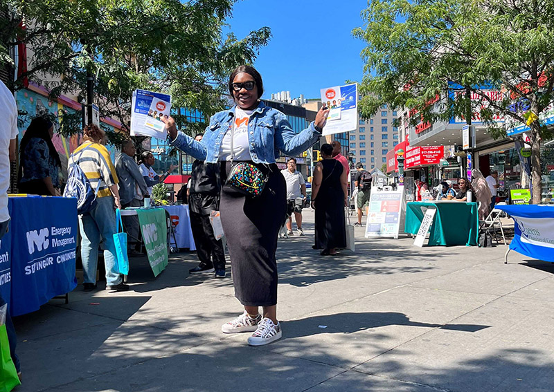 Woman stands outside holding flyers in each hand smiling at the camera