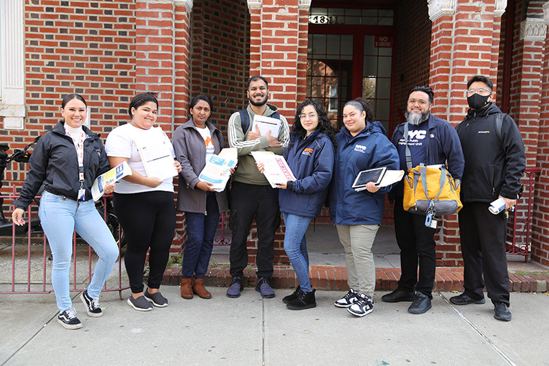 Group of PEU staff stand outside in front of a residential building holding tenant helpline and rent freeze flyers