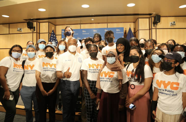 Mayor Eric Adams giving a thumbs up with a group of CUNY interns, all wearing Mayors PEU tee-shirts.