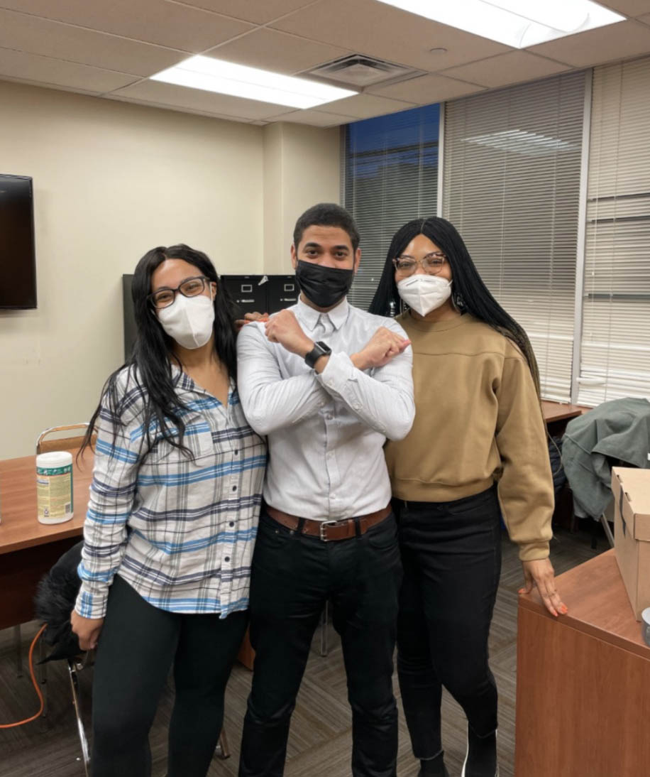 Three PEU staffers smiling, one holding up his arms with a symbol of the Bronx.