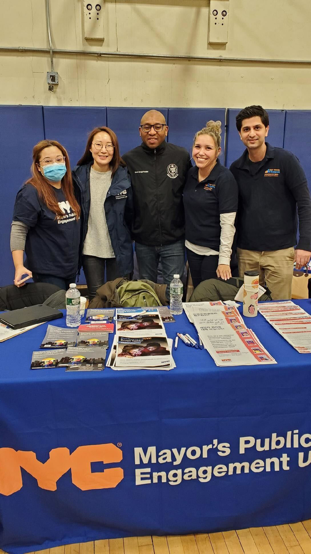 Four PEU Specialists stand with the Queens Borough President behind a table with flyers while smiling