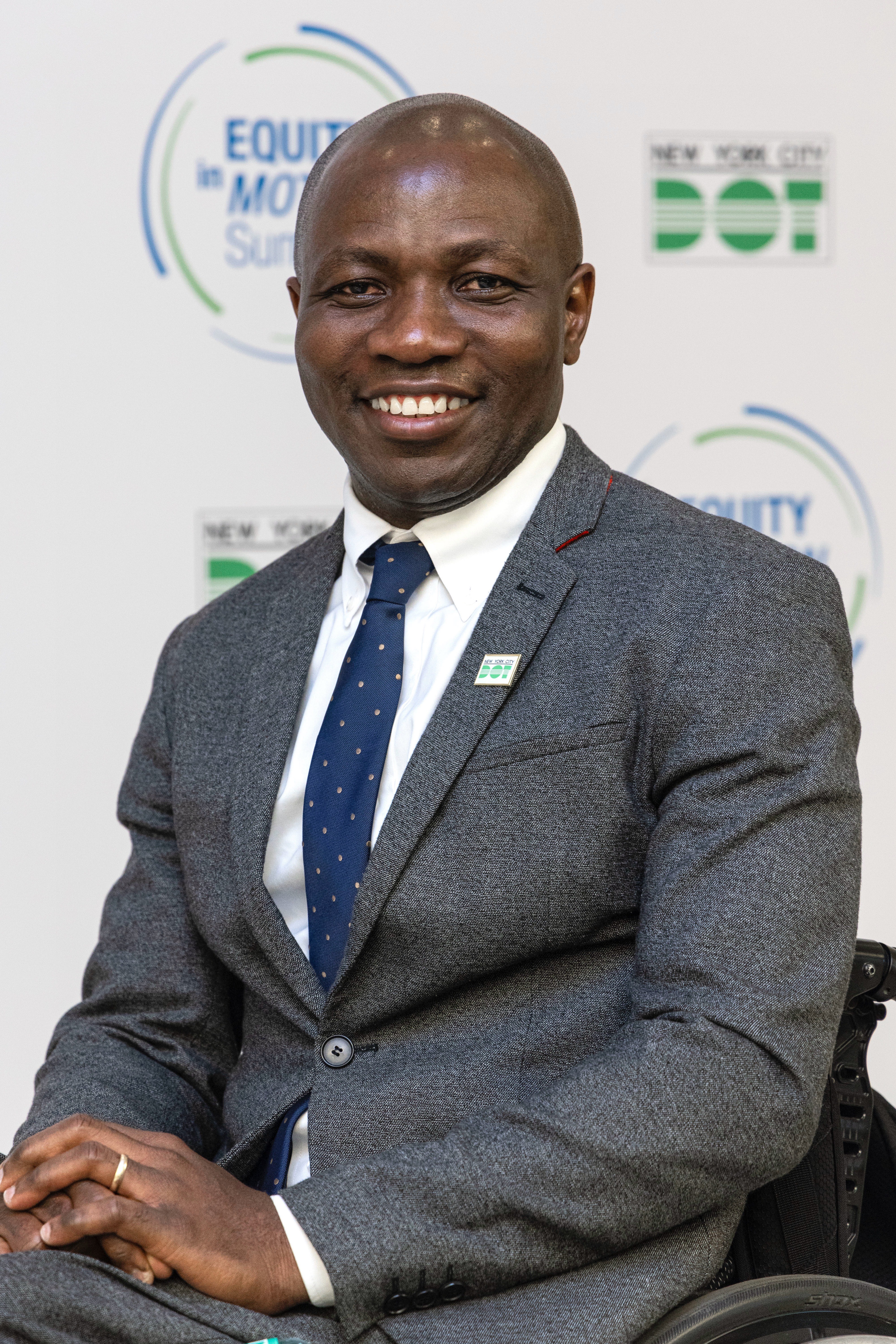 Edmund Asiedu, N Y C  D O T  D S F, seated in a wheelchair, wearing a suit with a big smile.