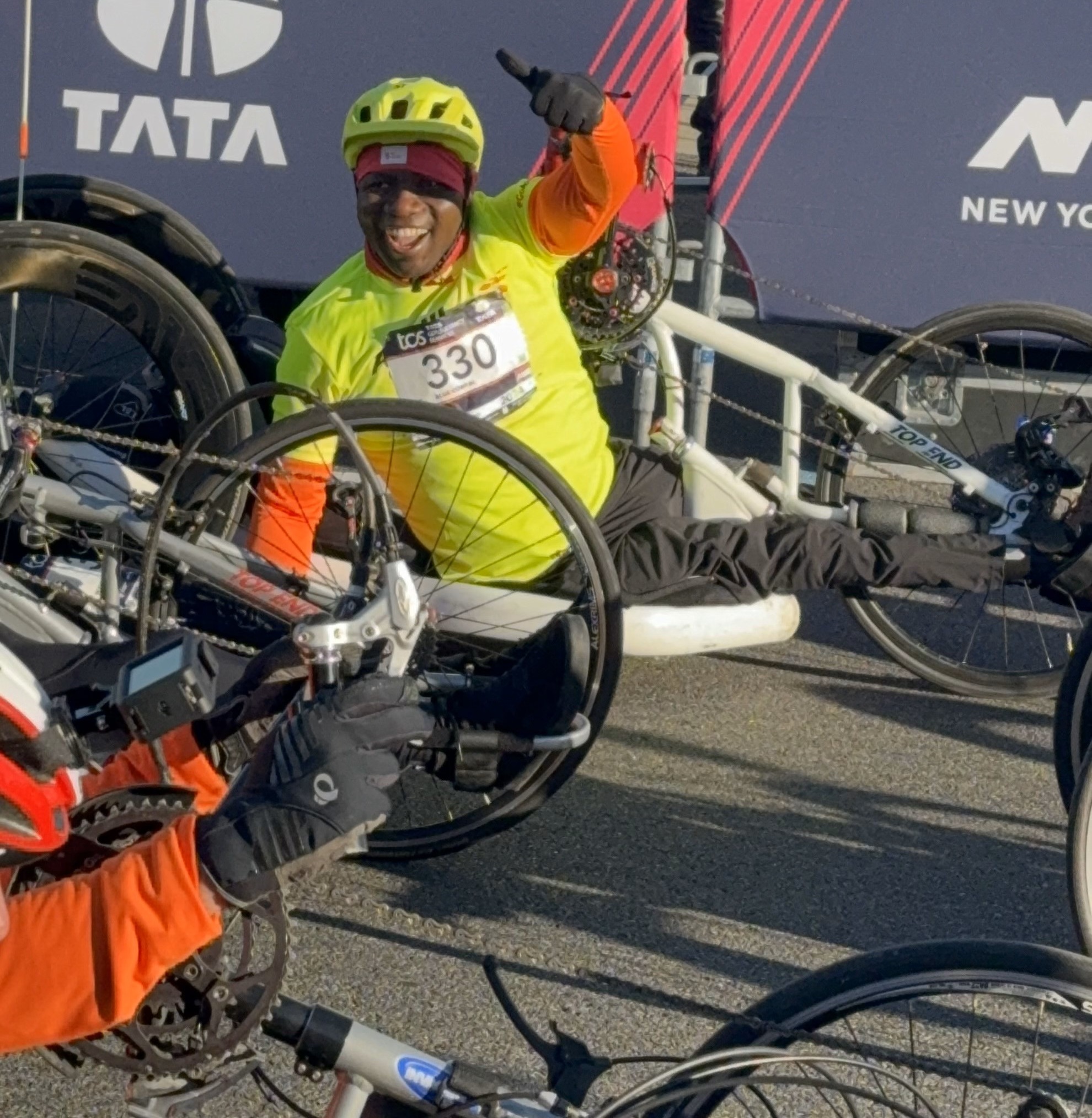 Edmund, seated in a handcycle and sporting a yellow jacket and racing bib, gives a thumbs up on race day.