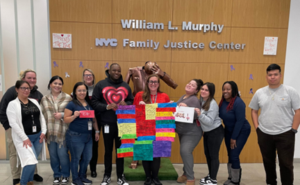 a group of people holding a makeshift LGBTQ+ flag and stands in front of the NYC Family Justice Center