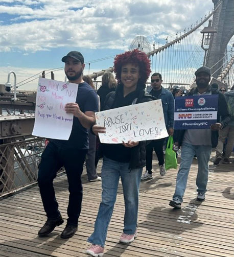 Two people walking on the Brooklyn Bridge holding signs saying No means no means no. Keep your hands to yourself and Abuse isn't love