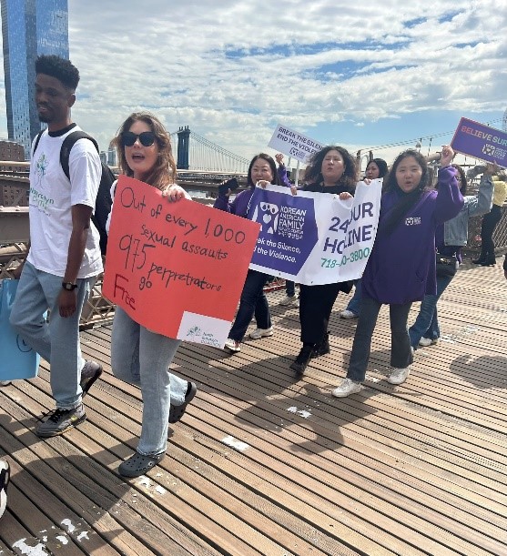 Large group of people dressed in denim marching across the Brooklyn Bridge pedestrian walkway.