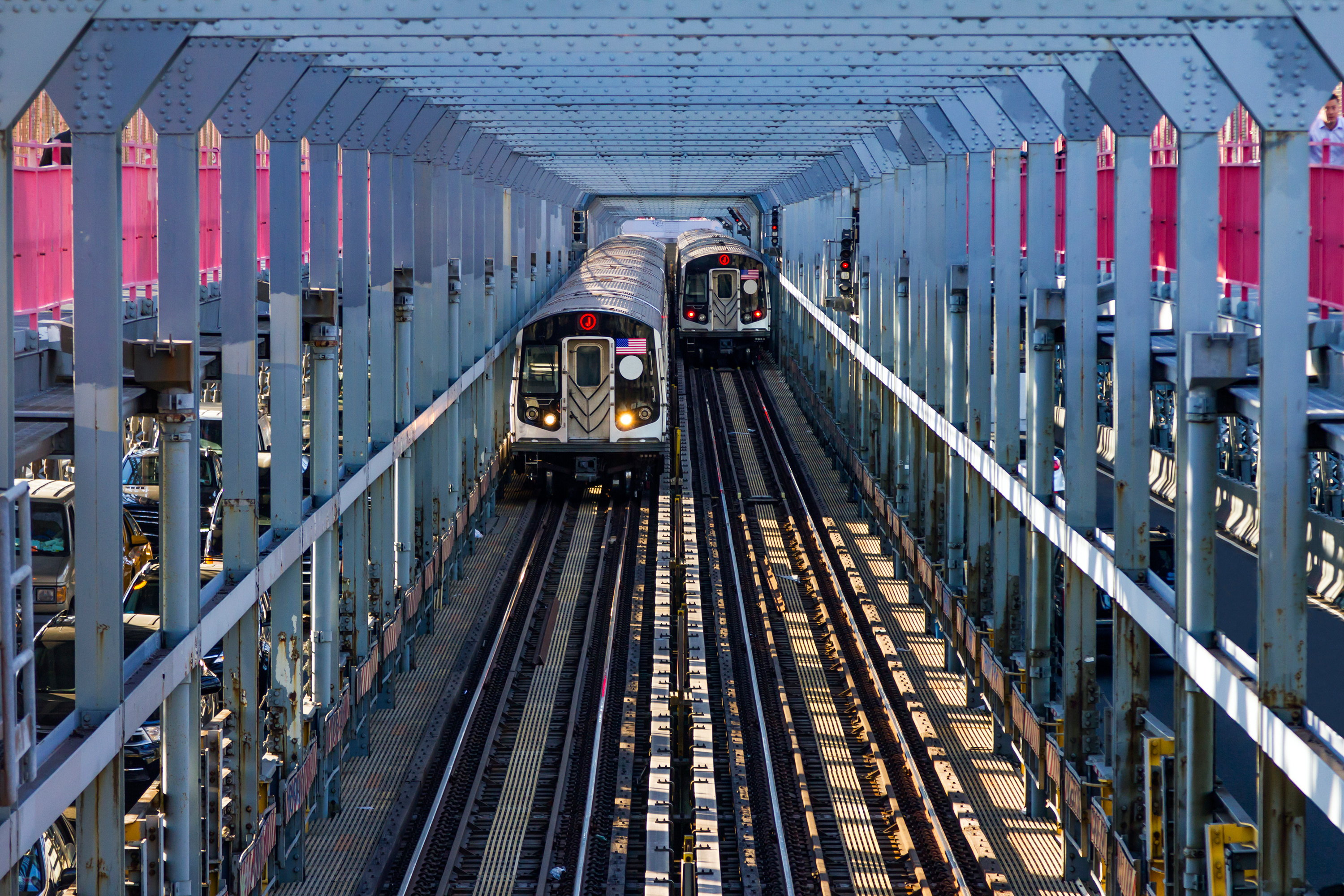 Picture of the Williamsburg Bridge at dusk. There is a subway train moving from Brooklyn toward Manhattan. The subway train is silver.
                                           