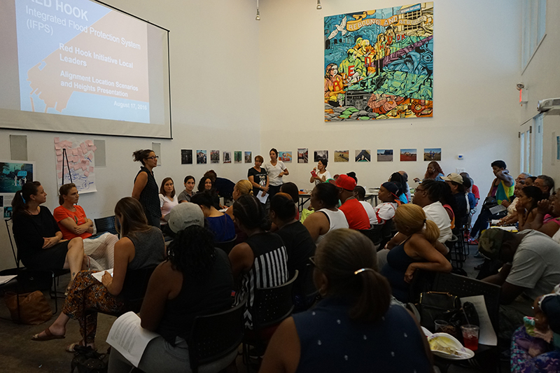 Group of people listening to woman standing at front of room giving a presentation