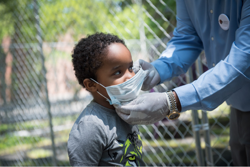 Photo of an adult helping a child put on a face mask