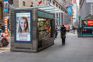 A newsstand on an N Y C sidewalk sells small goods like snacks  and magazines.