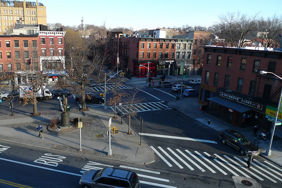 A quiet street next to a public space triangle in Brooklyn.