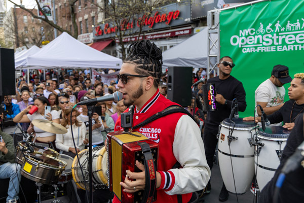 A musician sings into a microphone while playing a small accordion during a concern on a street closed to vehicles