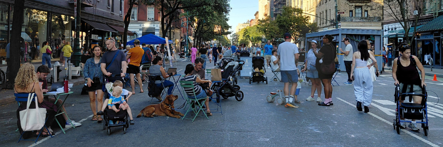 People site, walk, and stand together on a street temporarily closed to vehicular traffic and open for pedestrians.