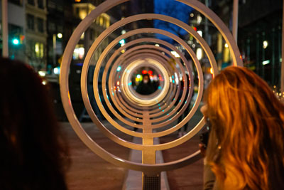 A series of rings illuminate at night in NYC as people talk into the art installation.